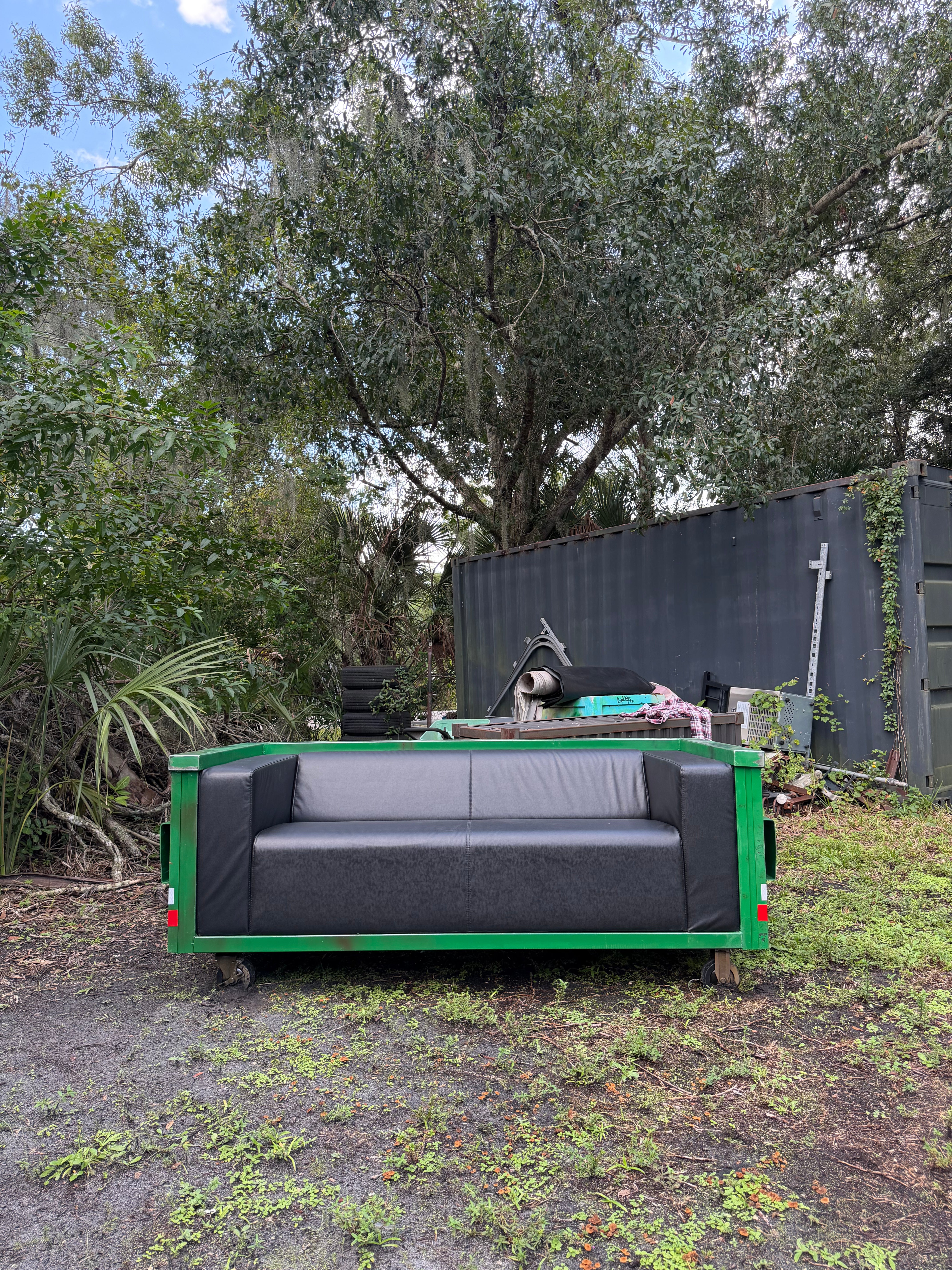 'Modular Waste' sofa, straight-on front view: black vegan leather seat and back cushions framed by green steel sides on casters