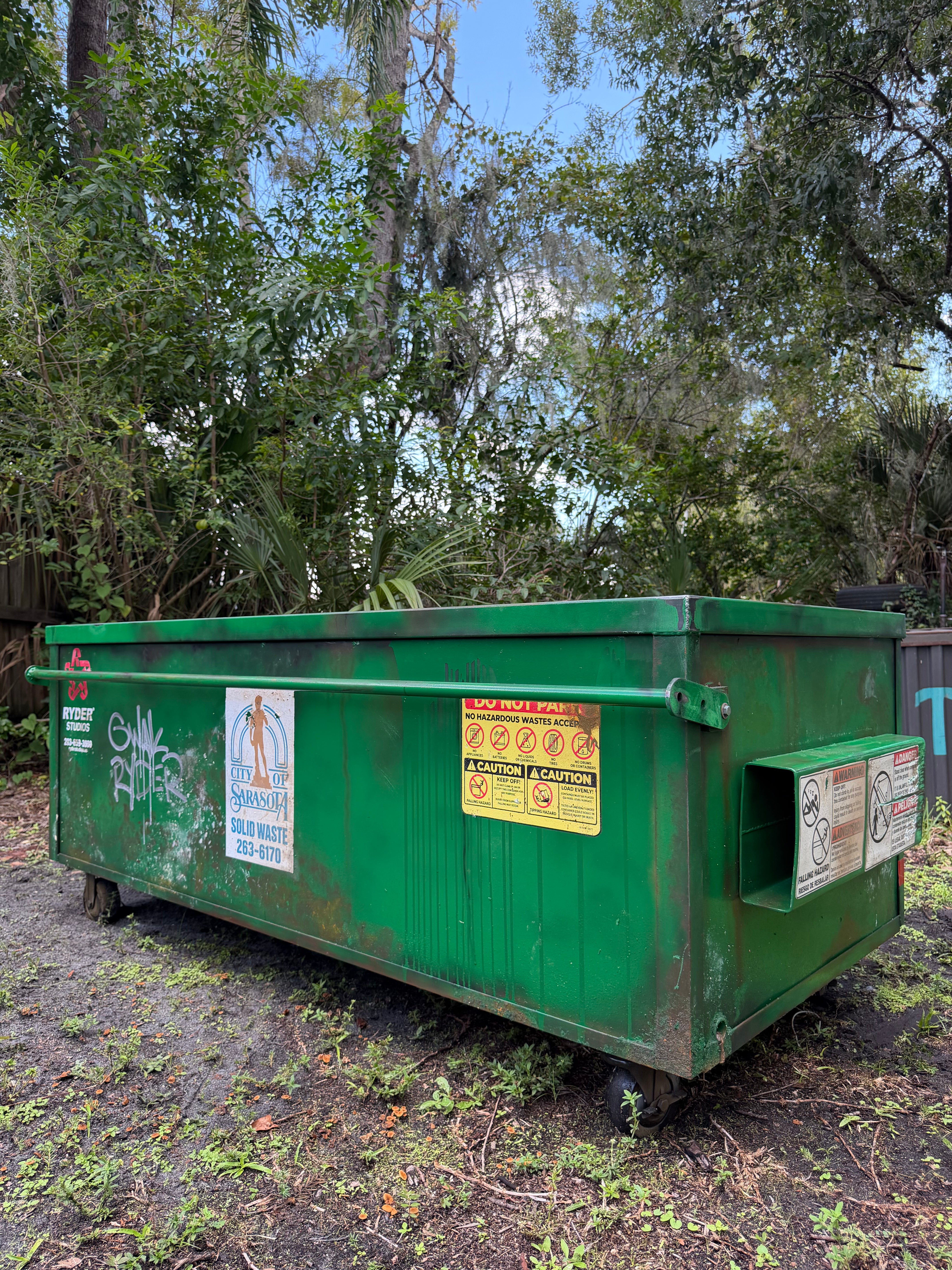 'Modular Waste' sofa, back view: hand-painted, aged green dumpster exterior with graffiti tag, municipal stickers, steel bar and caster wheels