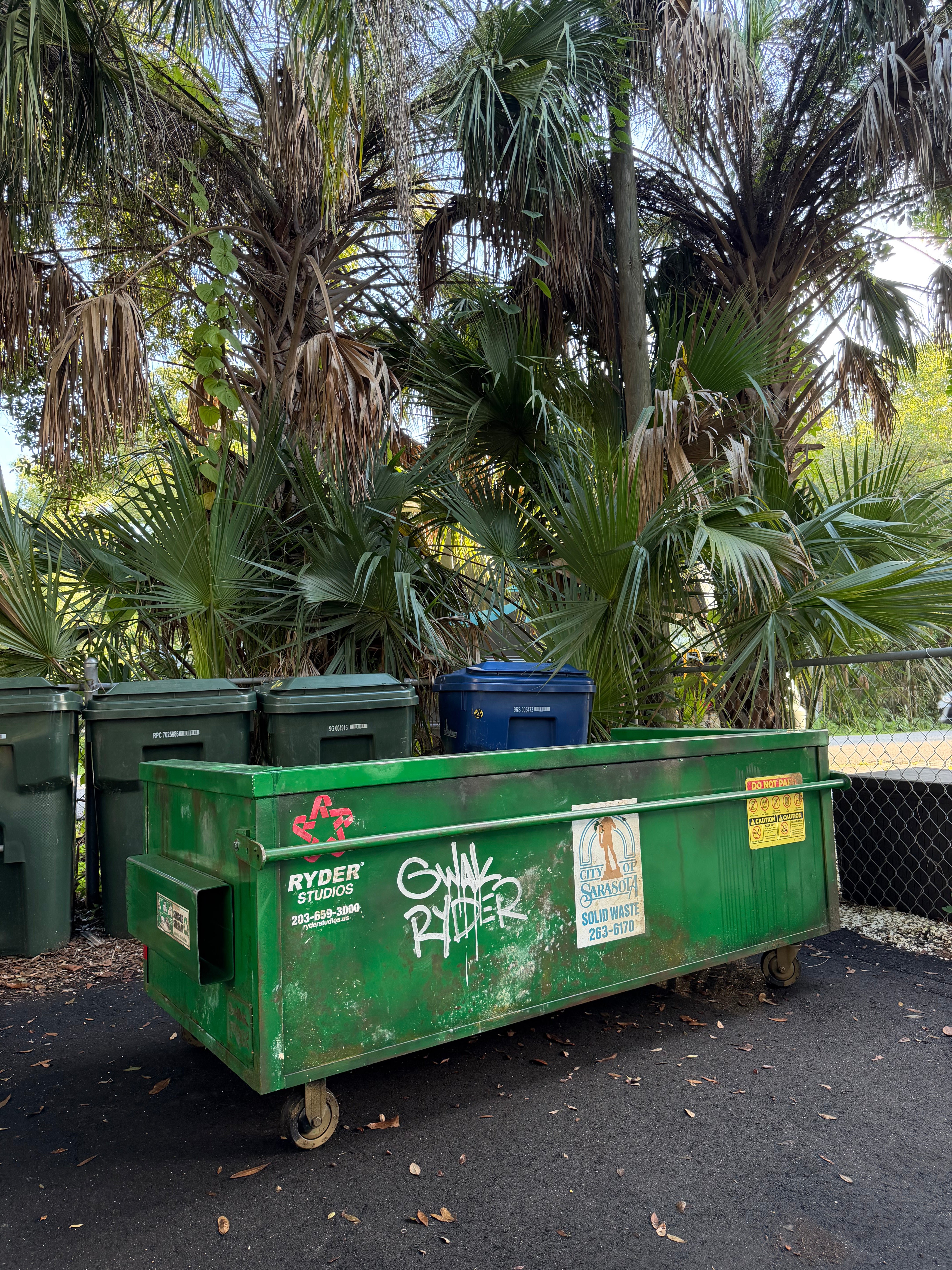 'Modular Waste' sofa, back view at an angle: hand-aged green dumpster exterior with Ryder Studios logo, graffiti tag, fork pocket and casters